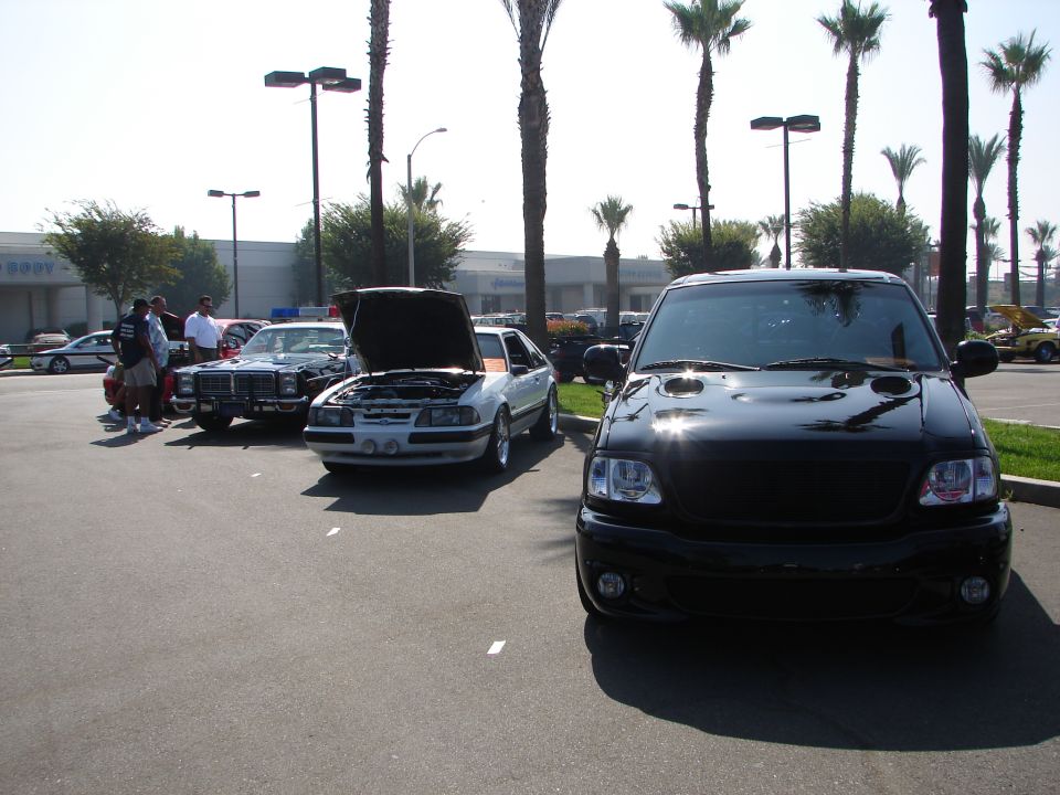 Black pickup truck front view, parked outdoors with palm trees and other cars