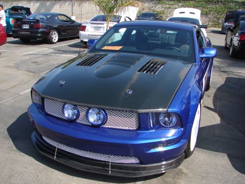 1992 Ford Taurus - A blue Ford Mustang with a custom carbon fiber hood and grille is parked at an outdoor event.