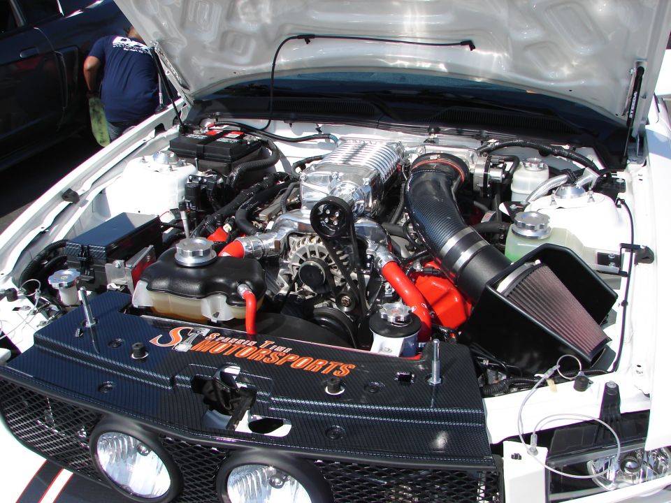 Engine bay with a supercharger, custom intake, and "ST Motorsports" branding on a black grille insert