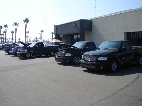 1992 Ford Taurus - A line of black Ford F-150 Lightning trucks are displayed, some with hoods open, at an outdoor event.