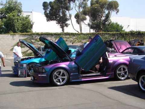 1992 Ford Taurus - Two custom Ford Mustangs with butterfly doors open are displayed at a car show. The purple and teal Mustang is in the foreground.