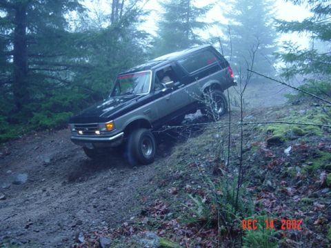 1989 Ford Bronco - 1989 Ford Bronco navigates a challenging off-road trail in a wooded area.