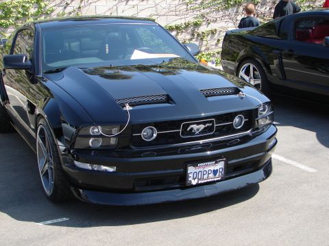1992 Ford Taurus - Black Ford Mustang with custom hood scoops and grille, parked next to another vehicle.