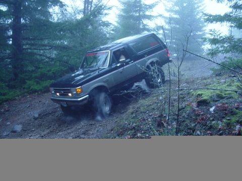 1989 Ford Bronco - A two-tone Ford Bronco navigates a steep, wet, and wooded trail.