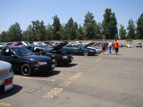 1992 Ford Taurus - Several cars are parked in a lot on a sunny day, with some hoods open.