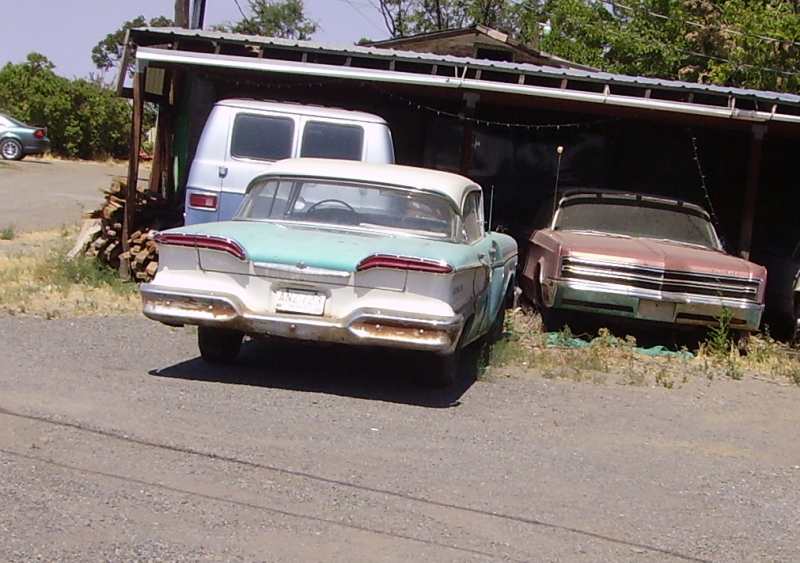 Two-tone 1958 Ford Fairlane sedan, rear view, dusty, with a van and another car