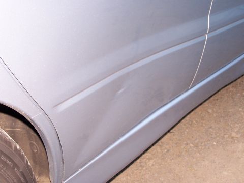 1995 Ford Probe - Close-up view of a dent on the side of a silver car, showing the door panel and lower molding.