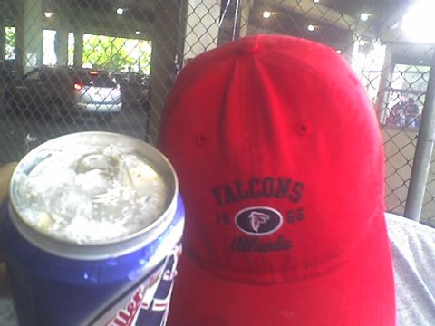 1989 BMW 3 Series - Person wearing an Atlanta Falcons cap holds a drink can in front of a chain-link fence.