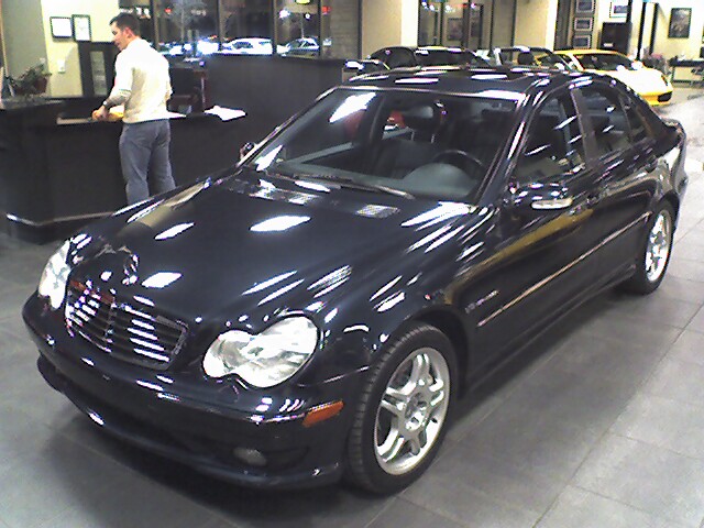 Dark sedan with chrome grille and multi-spoke wheels parked inside a showroom