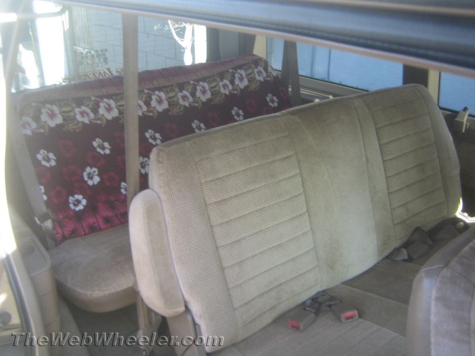 Tan fabric seats with seatbelts and a floral patterned seat cover in the rear