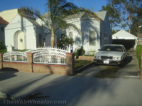 1968 Ford Mustang - A white sedan is parked in the driveway of a house, with a white fence in the foreground.
