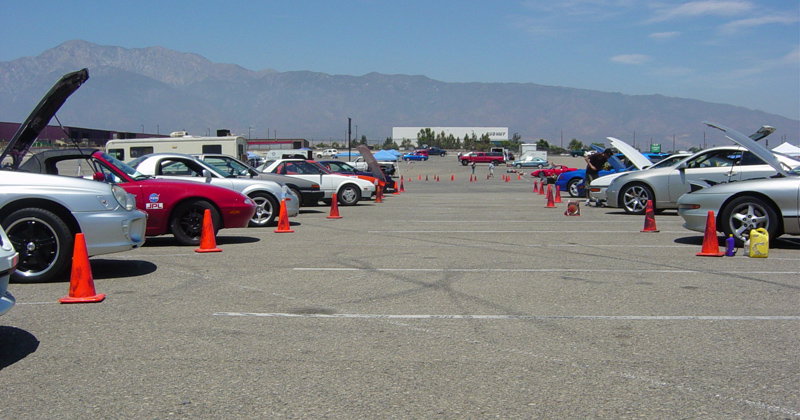 Several cars parked on a lot with orange cones, mountains in the background
