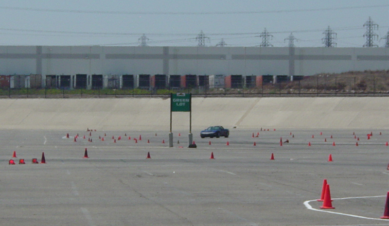 Blue coupe driving through cones on a race track with a 'Green Lot' sign