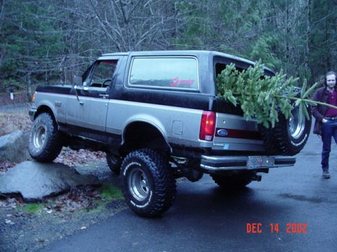 1989 Ford Bronco - A two-tone Ford Bronco with off-road tires is seen with a Christmas tree in its cargo area.