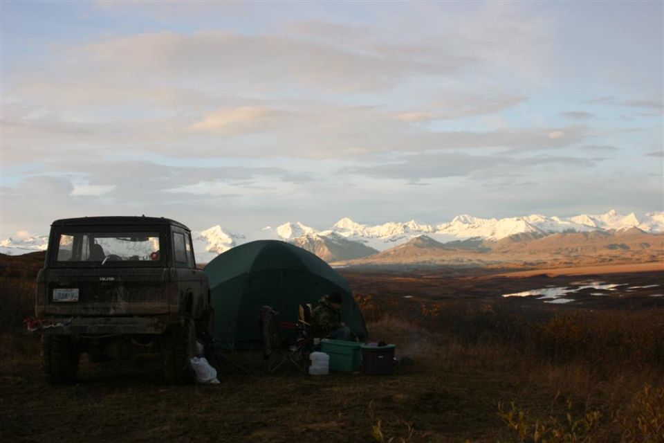 Dark SUV parked next to a tent with snow-capped mountains in the distance