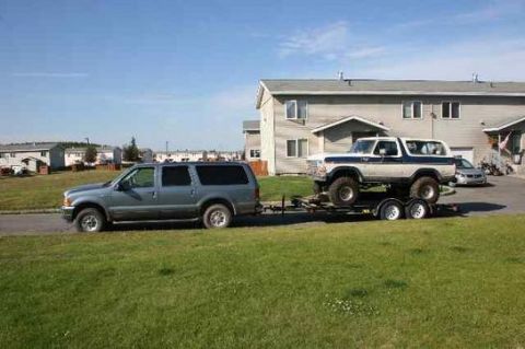 1978 Ford Bronco - A 1978 Ford Bronco is transported on a trailer, towed by a grey SUV in front of a residential building.