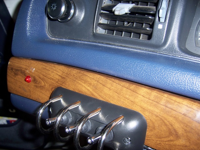 Dash close-up: woodgrain panel with four chrome toggle switches and red light below blue dash and air vent