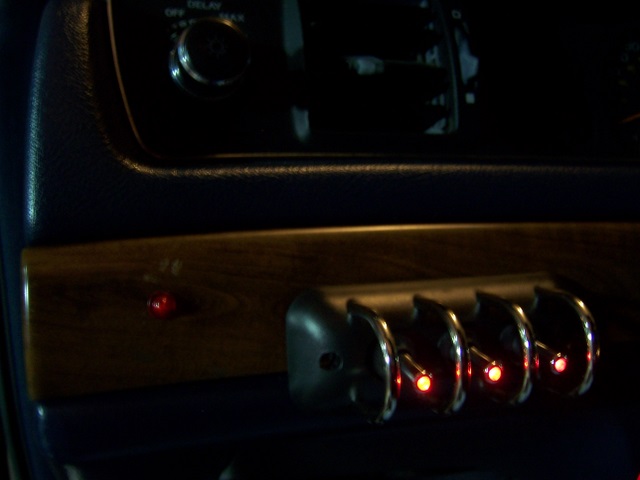 Dark car dash with woodgrain trim, chrome switches lit with red indicator lights