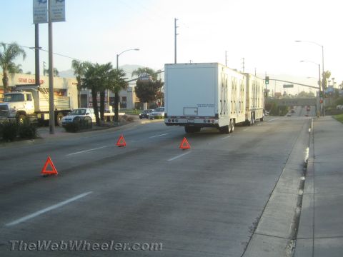 1990 Ford Bronco - white box semi-trailer stopped on a city street with reflective warning triangles placed on the pavement behind it.