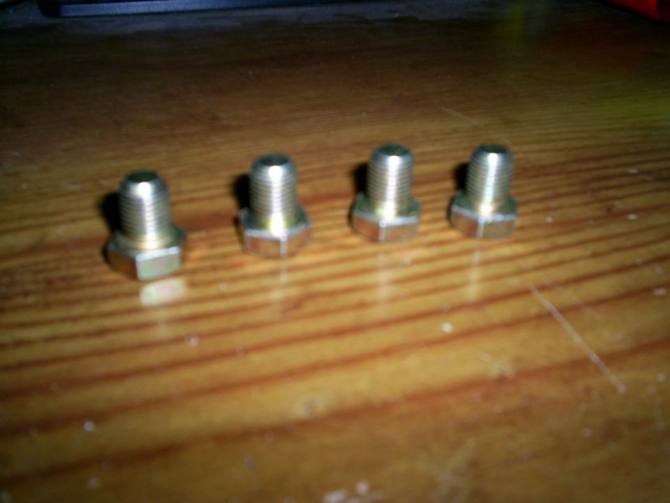 Four hex-head bolts with threaded shafts on a wooden surface