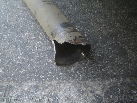 1990 Ford Bronco - metal driveshaft tube lying on asphalt with one end torn and sheared open from failure.