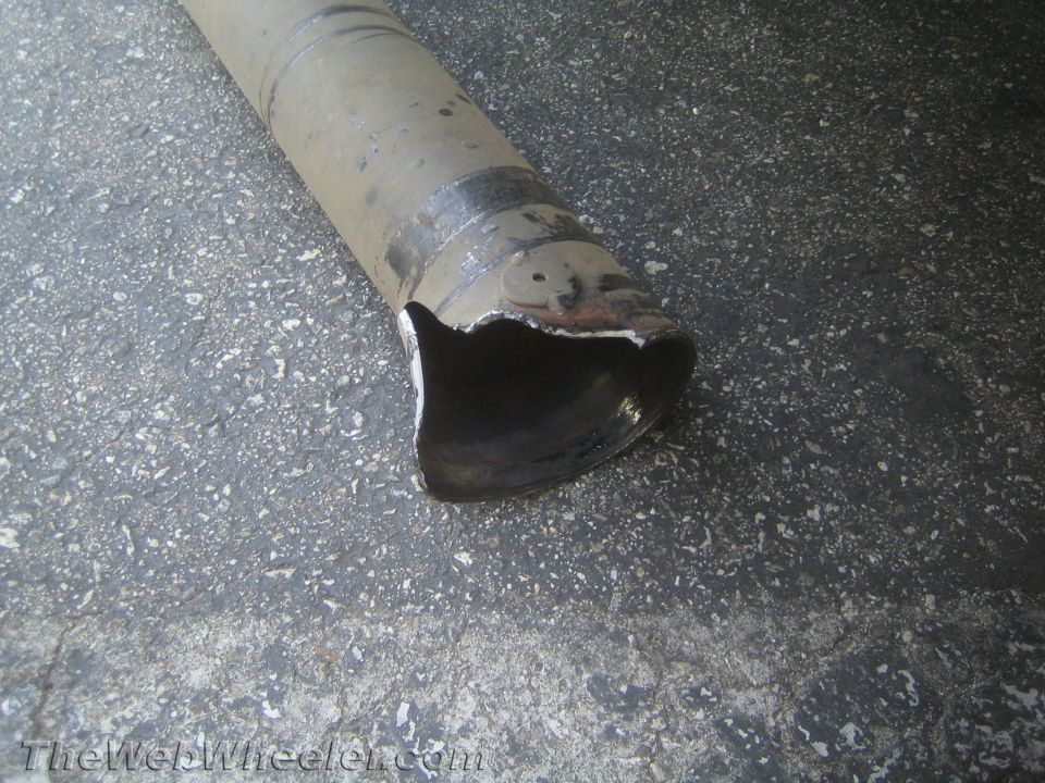 metal driveshaft tube with a torn, sheared-off end lying on pavement