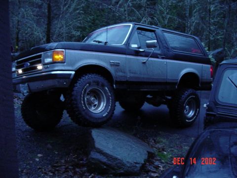 1989 Ford Bronco - A lifted Ford Bronco is parked on rocks with trees in the background. A date stamp is visible.