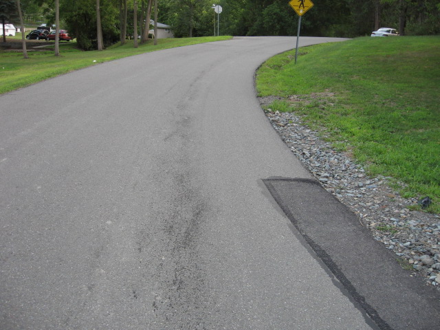 Road curves uphill with parked cars on the left and a white sedan on the right
