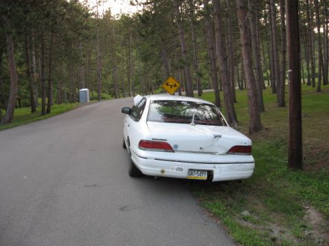 1992 Ford Crown Victoria - A white 1992 Ford Crown Victoria is parked on the shoulder of a rural road, surrounded by trees.