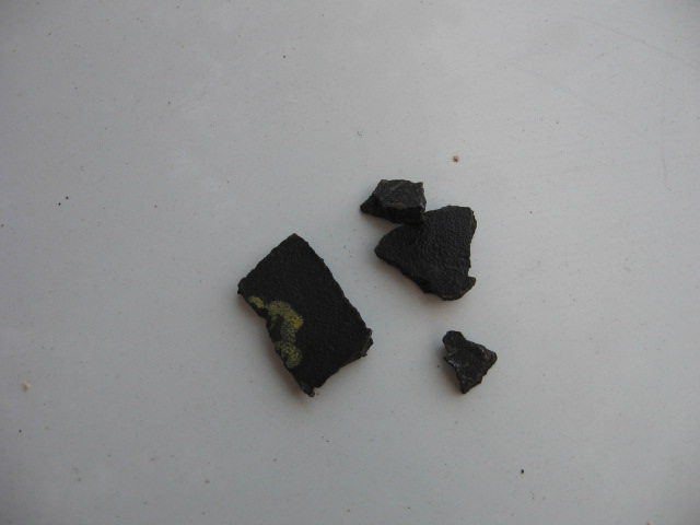 Several fragments of black material, one with yellow markings, on a white surface