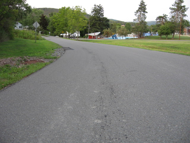 Empty road leading towards houses and a park with a swimming pool
