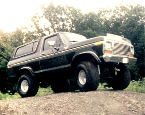 1979 Ford Bronco - This lifted 1979 Ford Bronco is shown in a three-quarter front view, parked on a dirt path with trees in the background.