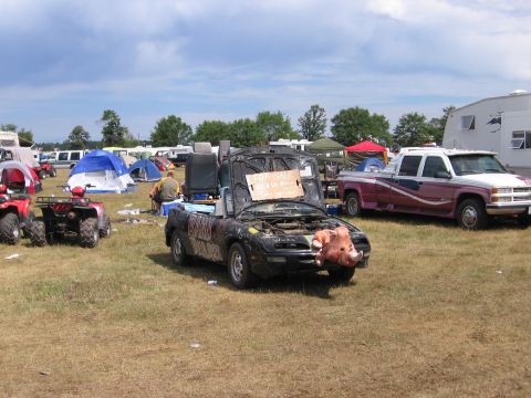 1998 GMC Sierra 1500 - A heavily modified convertible with a pig decoration is parked in a field with tents and other vehicles.