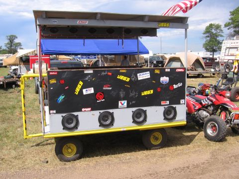 1998 GMC Sierra 1500 - A custom trailer with multiple speakers and various stickers is parked outdoors with other vehicles and tents.