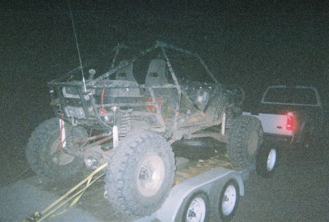 1984 Ford Bronco - An off-road buggy is secured to a trailer, with a pickup truck visible in the background at night.