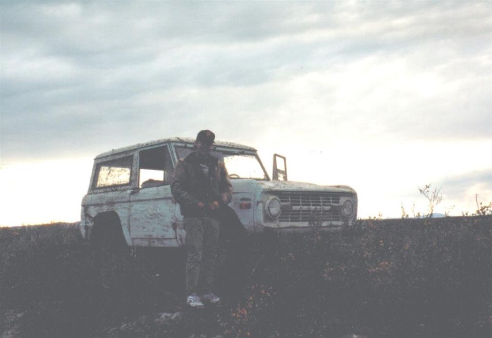 Man in camouflage stands by a white 1978 Ford Bronco with a dented front end