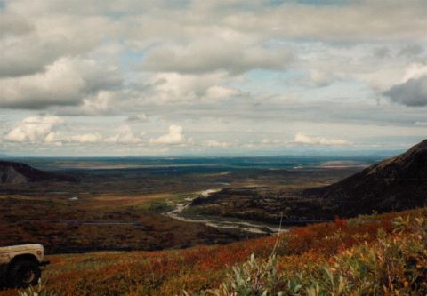 1978 Ford Bronco - A vehicle sits on a grassy hillside, surveying a broad, undeveloped valley with a river cutting through the terrain.
