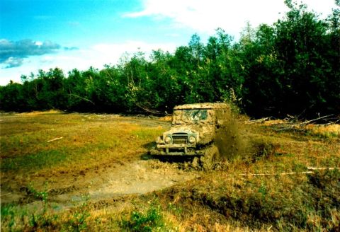 1978 Ford Bronco - A heavily muddied off-road vehicle navigates a challenging muddy terrain, kicking up dirt and water.