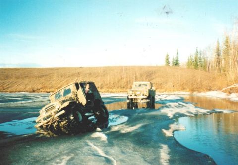 1978 Ford Bronco - Two off-road vehicles traverse a partially frozen waterway under a clear blue sky.