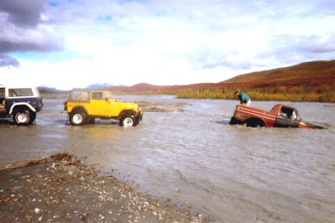 1978 Ford Bronco - Three off-road vehicles navigate a shallow river during an autumn day.