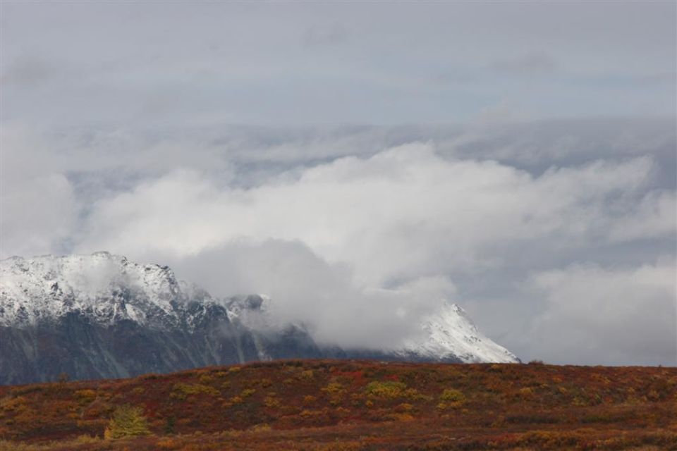 Mountain landscape with snow-capped peaks and autumn foliage under cloudy sky