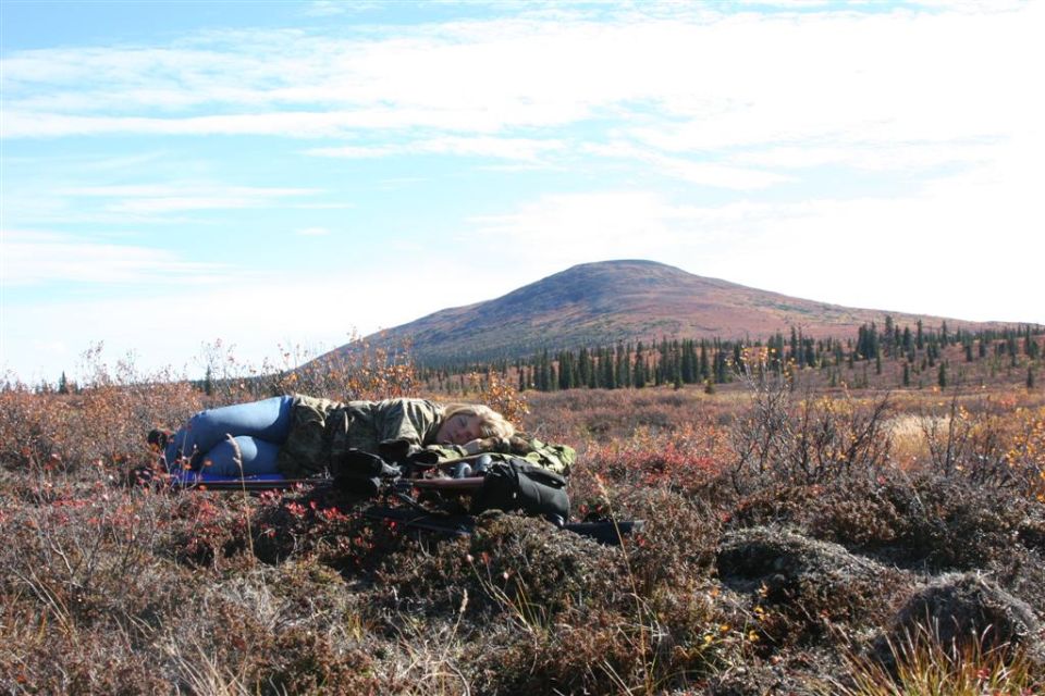 Person sleeping outdoors in a field with a mountain in the background
