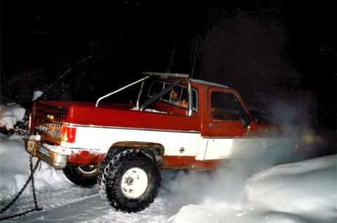 1978 Ford Bronco - A two-tone pickup truck is stuck in the snow, with chains attached to the rear bumper.