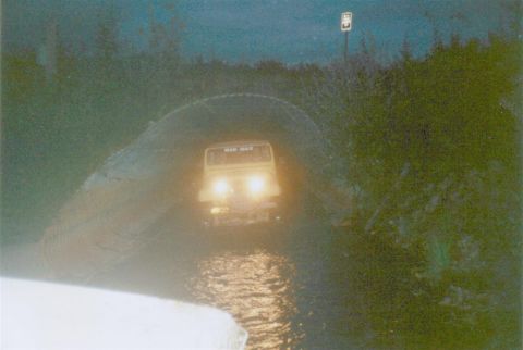 1978 Ford Bronco - A yellow SUV, possibly modified with 'MAD MAX' branding, drives through a flooded area at night.
