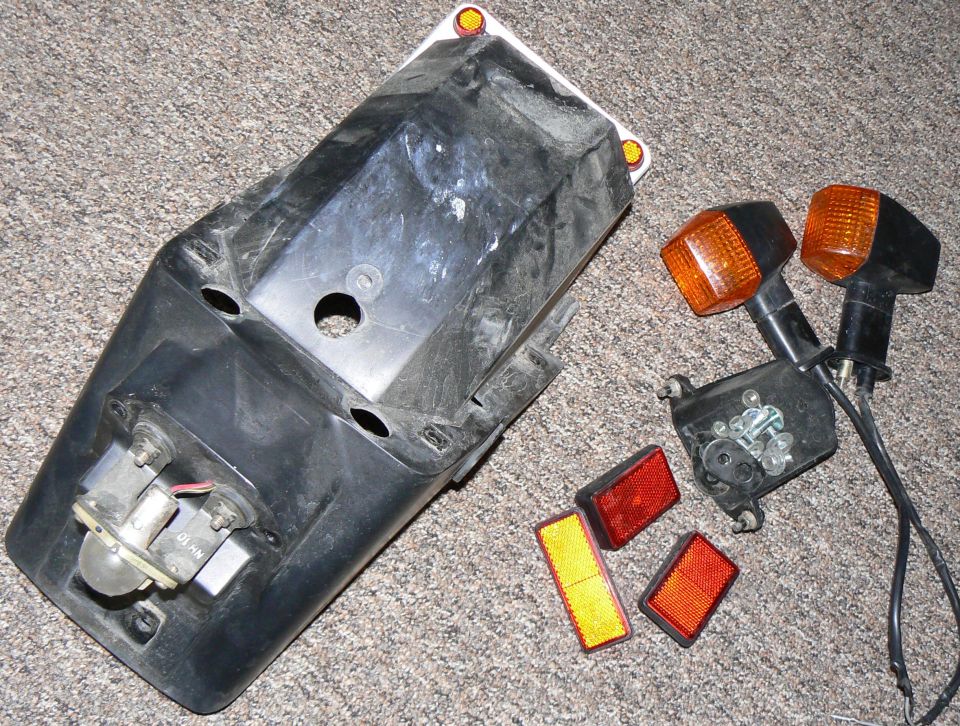 Black motorcycle fender with detached orange turn signals and red/yellow reflectors