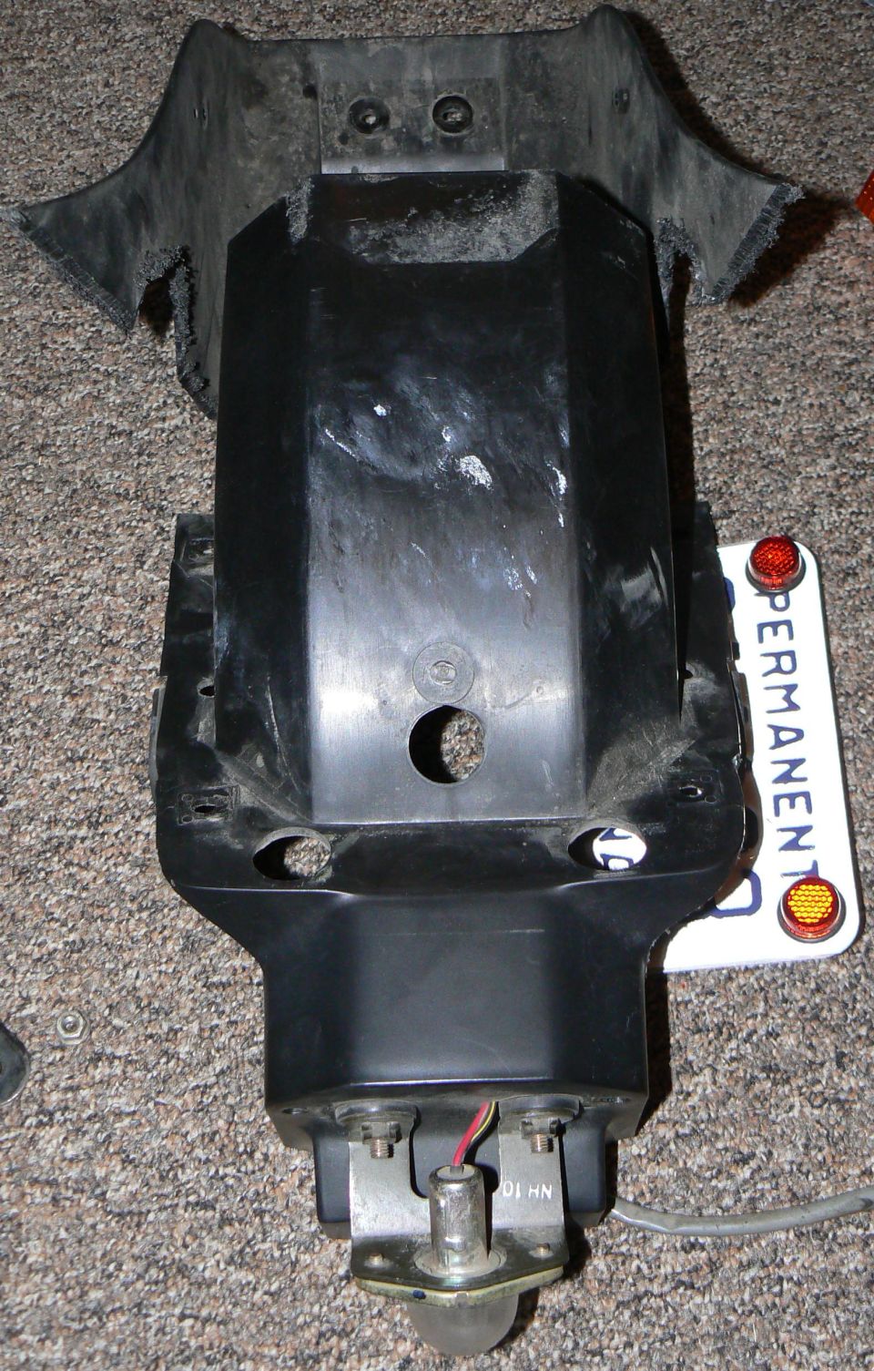 Motorcycle tail section with black plastic cover and a "PERMANENT" license plate attached