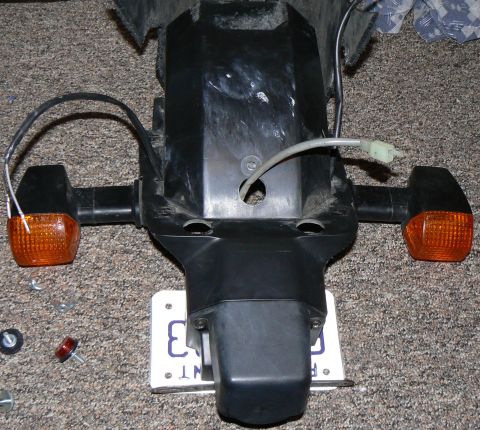 2002 Kawasaki Ninja - This is a close-up of a motorcycle's rear section, including turn signals and a license plate, lying on a carpeted surface.