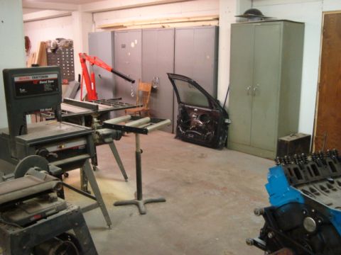 2000 Ford Crown Victoria - A detached car door is visible in a workshop setting, surrounded by various tools and equipment, including a band saw and an engine block.