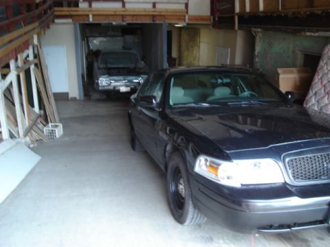2000 Ford Crown Victoria - Black 2000 Ford Crown Victoria in garage, another vehicle visible in background.