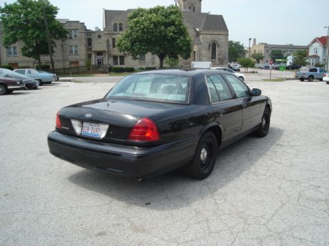 2000 Ford Crown Victoria - A black 2000 Ford Crown Victoria is parked in a lot with buildings and trees visible.
